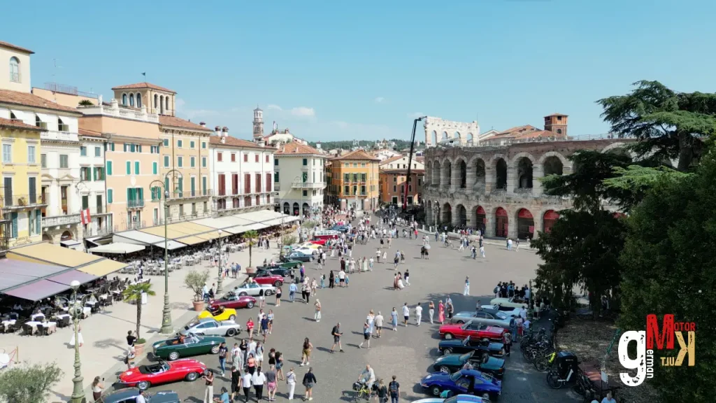 Oldtimer-Rallye auf historischem Platz in Verona mit Sportcabs und Klassikern vor römischem Amphitheater und Stadtpalazzi