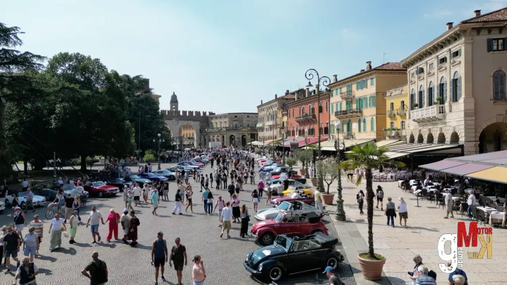 Oldtimer-Fahrzeuge präsentieren sich auf einem italienischen Marktplatz während einer Oldtimer-Rallye mit historischen Gebäuden und Besuchern