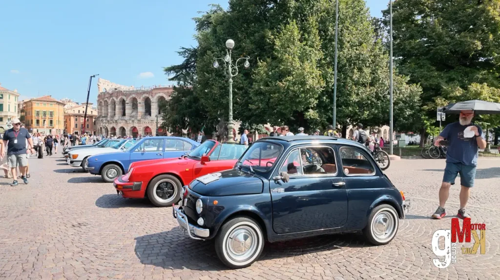 Mehrere Oldtimer-Fahrzeuge parken auf einem Platz vor historischer Architektur während der ADAC Gardasee Klassik, Zuschauer beobachten die Rallye