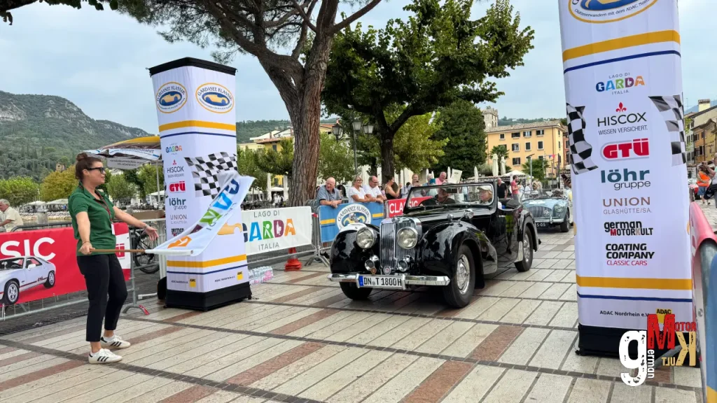 Oldtimer-Cabriolet fährt bei der ADAC Gardasee Klassik durch einen italienischen Platz mit Sponsorenbannern und Zuschauern