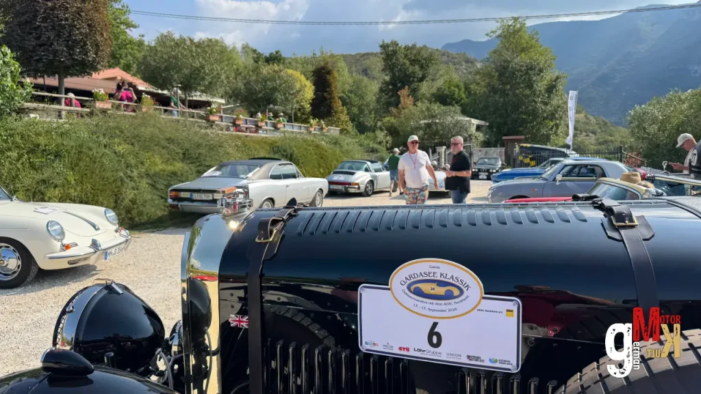 Schwarzer Oldtimer-Roadster mit Startnummer auf einem Veranstaltungsgelände, umgeben von weiteren Klassikfahrzeugen und Teilnehmern der ADAC Gardasee Klassik