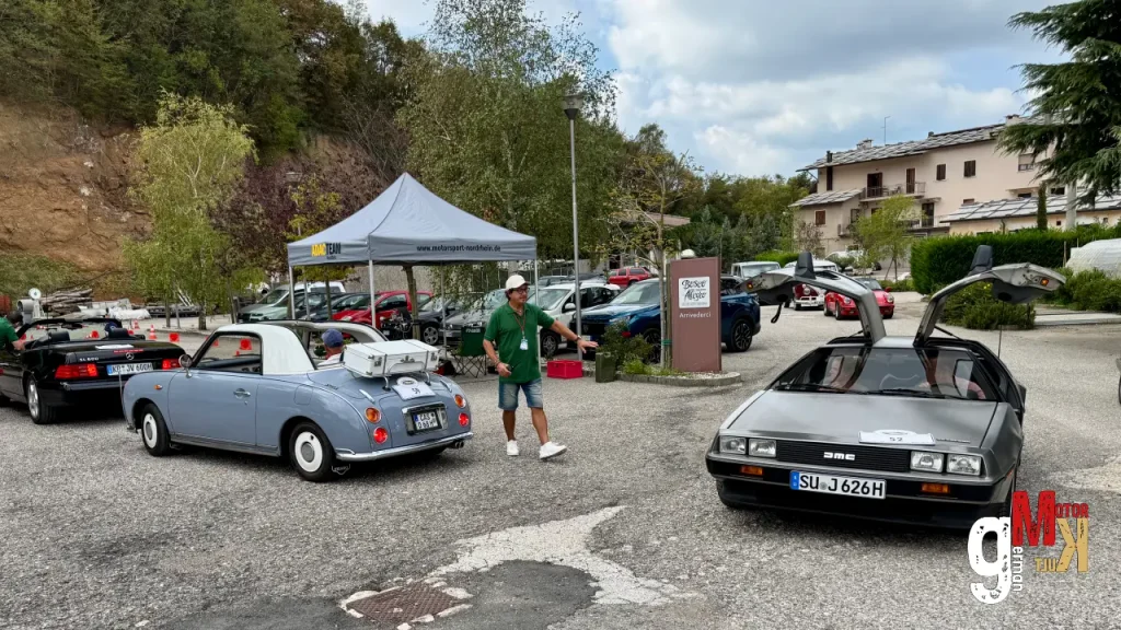 Oldtimer-Cabriolets und Limousinen parken auf einem Veranstaltungsgelände bei der ADAC Gardasee Klassik, im Hintergrund ein Informationszelt und Teilnehmer