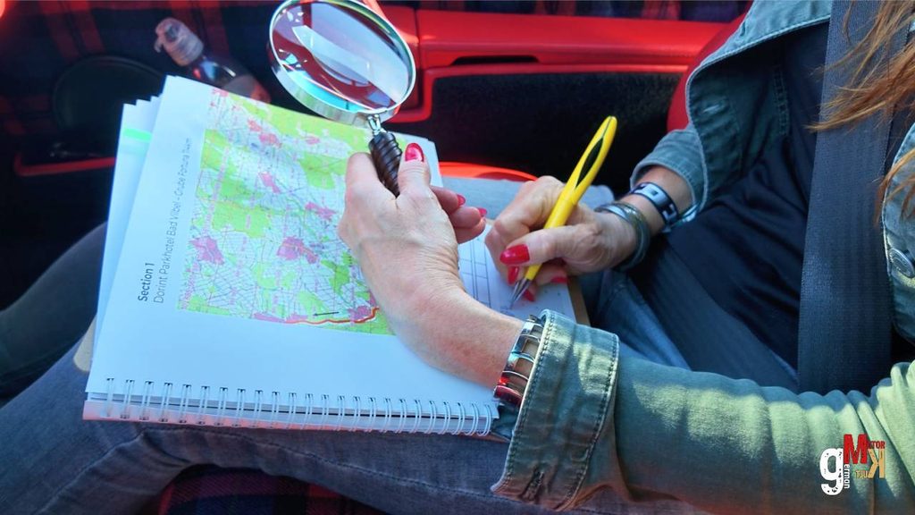 Rallyefahrer studiert Streckenkarte mit Lupe im Cockpit eines roten Oldtimers während der Club Rallye Taunus